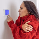 2_Freezing-woman-at-home-wears-sweater-and-tries-to-raise-the-temperature-on-thermostat-while-energy.avif