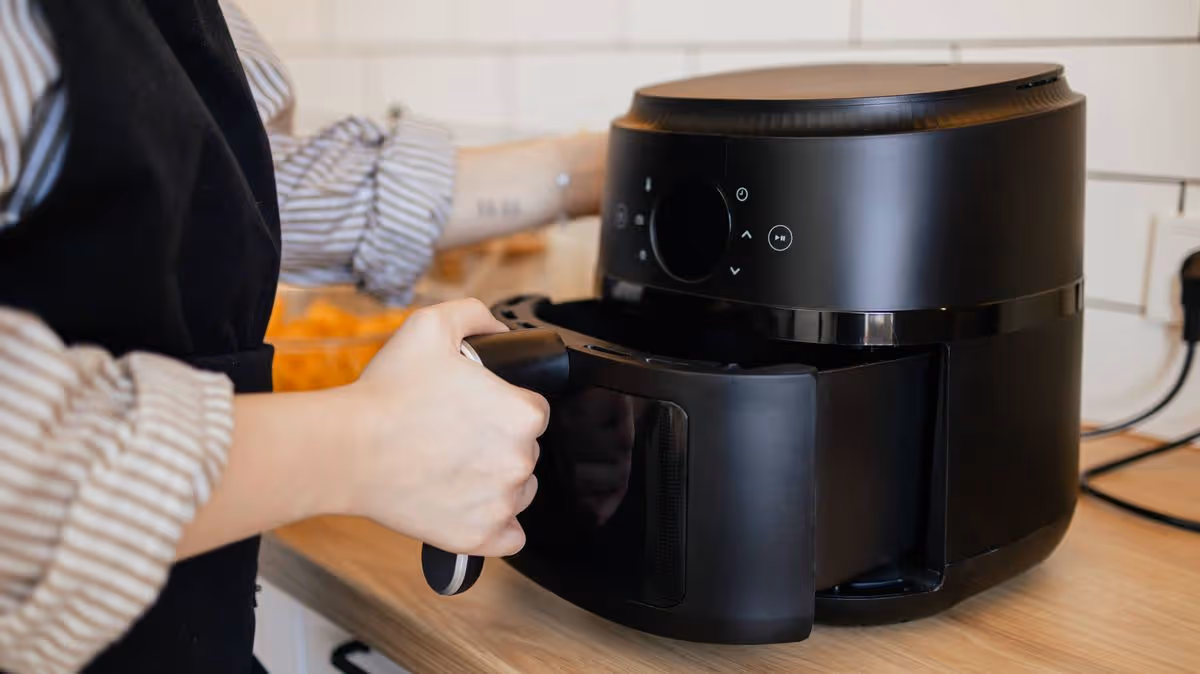0_Close-up-view-of-a-woman-putting-a-basket-into-an-air-fryer-for-cooking.jpg